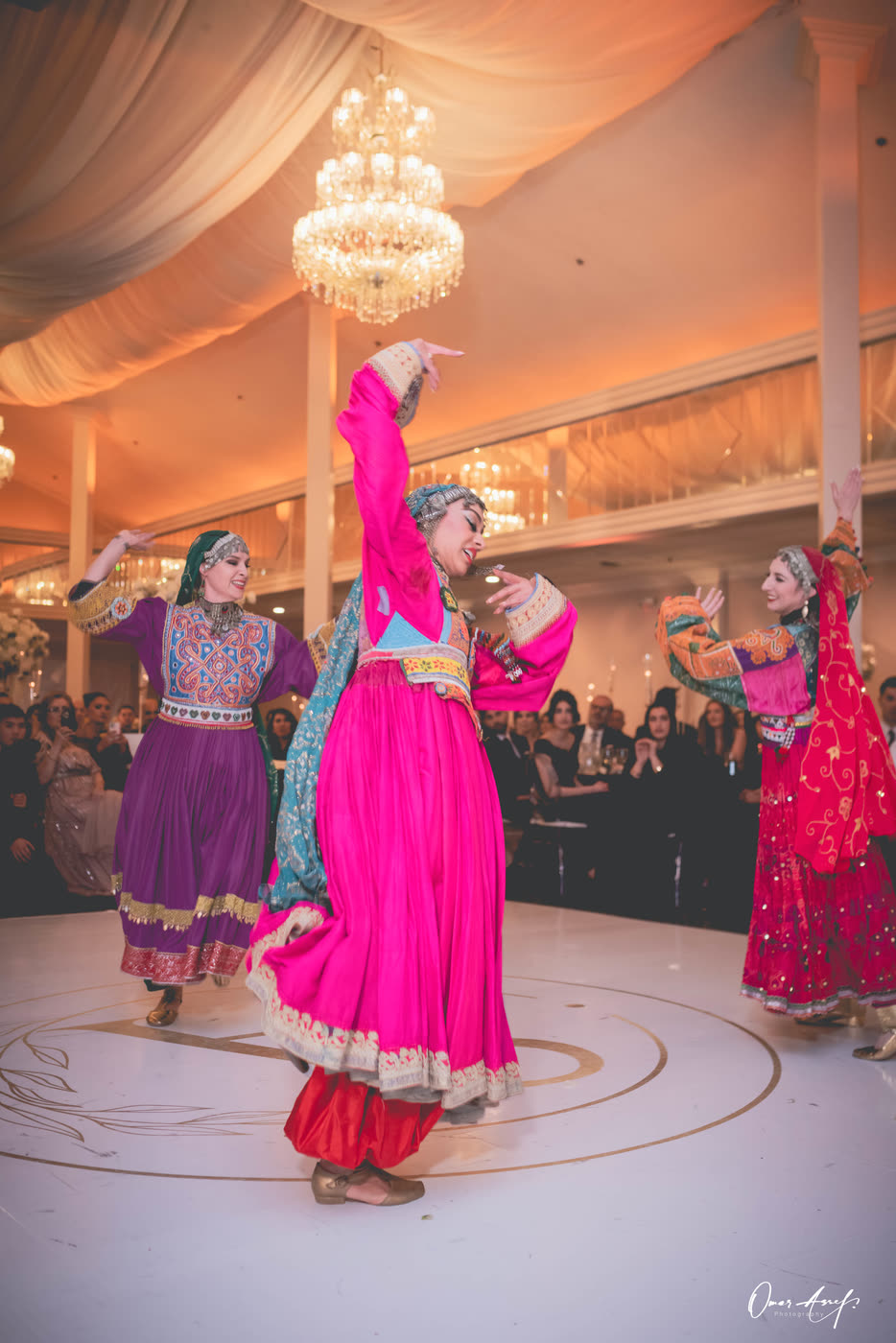 A dancer in magenta and turquoise turning under a chandelier